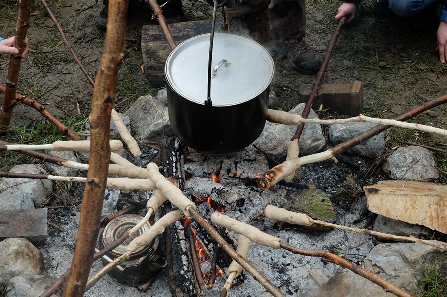 Stockbrot und Kochtopf über der Glut eines Lagerfeuers