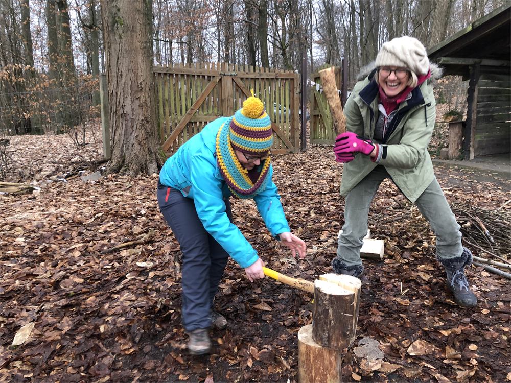 Zwei Frauen spalten lachend Holz im Winterwald