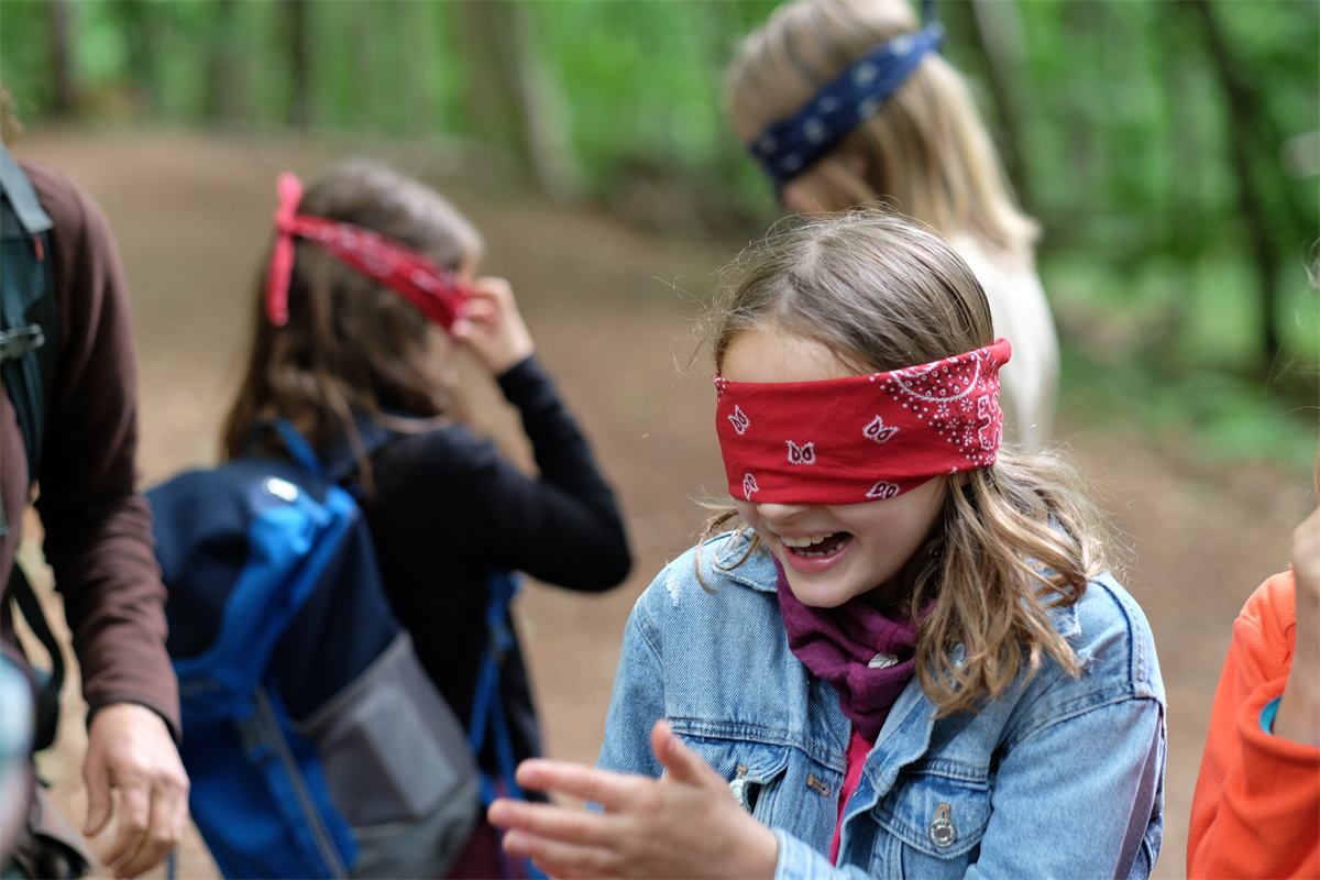 Lachendes Mädchen mit roter Augenbinde bei einem Waldspiel